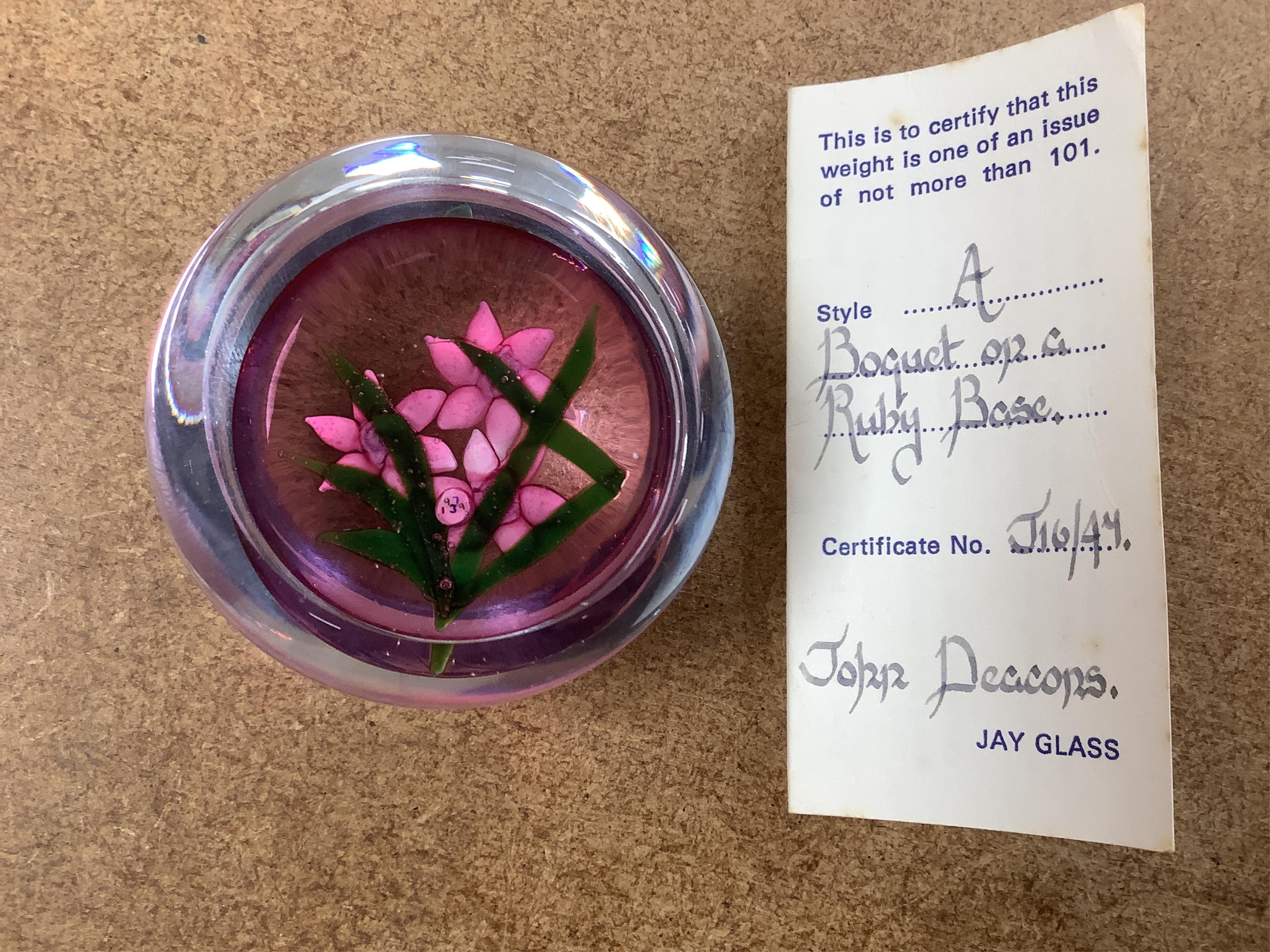Two Perthshire lamp work glass paperweights, fruit weight, 52/350, rose and bud weight, 69/300 together with a John Deacons bouquet on a ruby base paperweight, edition of 101 (3)